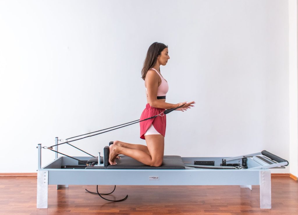 side view of a woman in activewear doing pilates reformer exercise